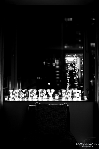 a lighted marry me sign with candles on a window just before saying yes