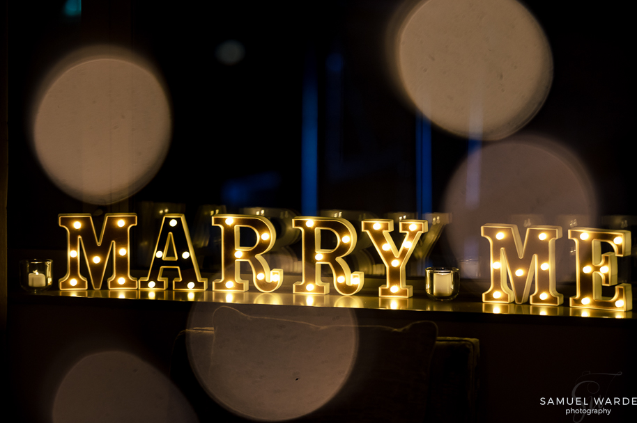 a lighted marry me sign with candles just before saying yes to forever